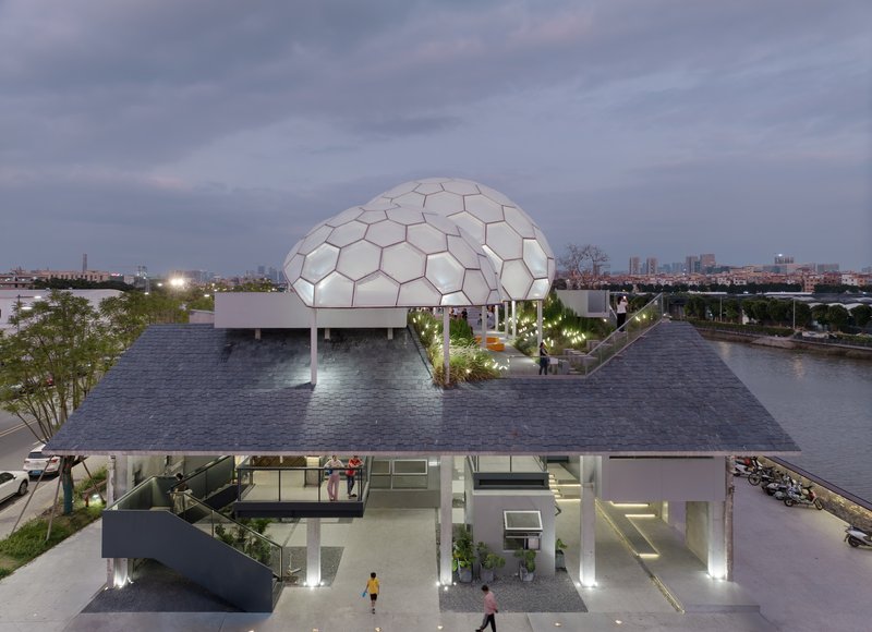 Elevated riverside platform with geodesic dome and glass-enclosed pavilion illuminated at dusk
