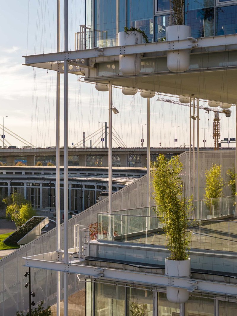 Cantilevered terraces with planters and cable suspension system above highway infrastructure at dusk