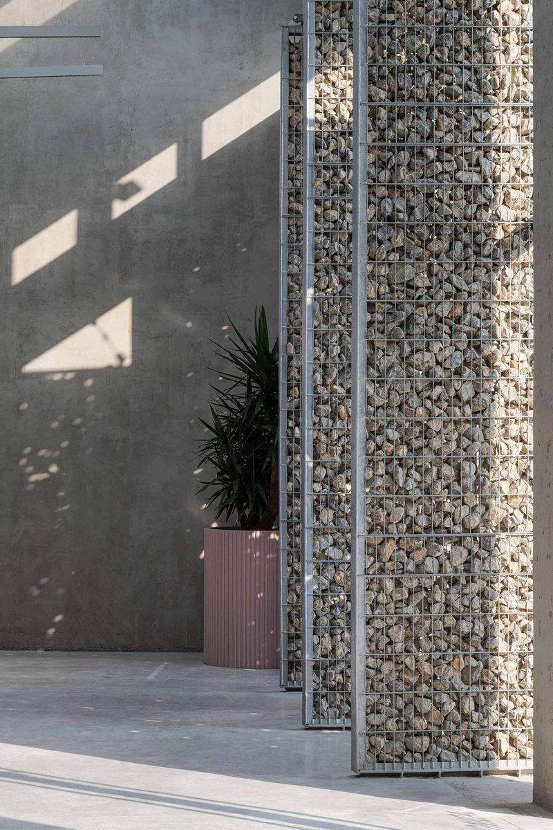 Gabion wall column filled with pale stones beside a potted plant in afternoon shadow