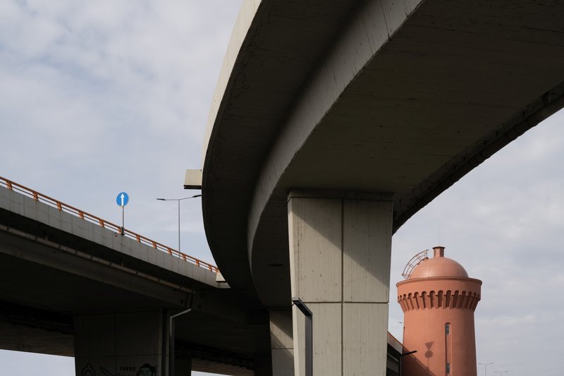 Concrete highway flyover piers with a terracotta water tower visible in the distance