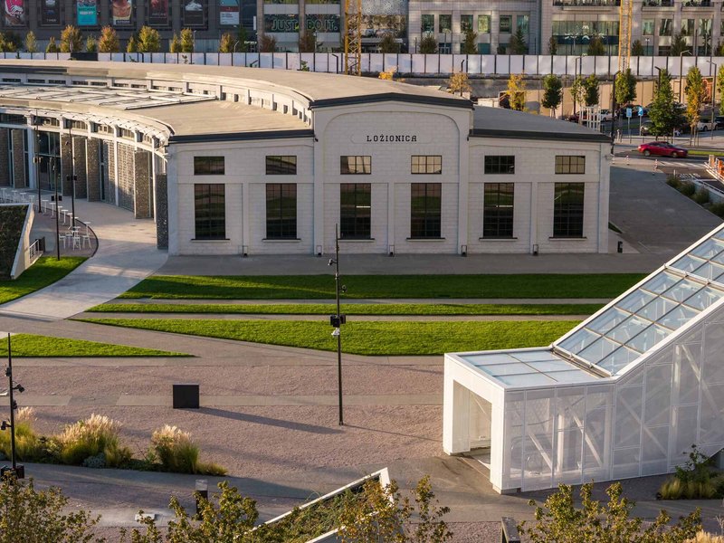 Aerial view of a white stucco building with tall arched windows framed by curving glass pavilions