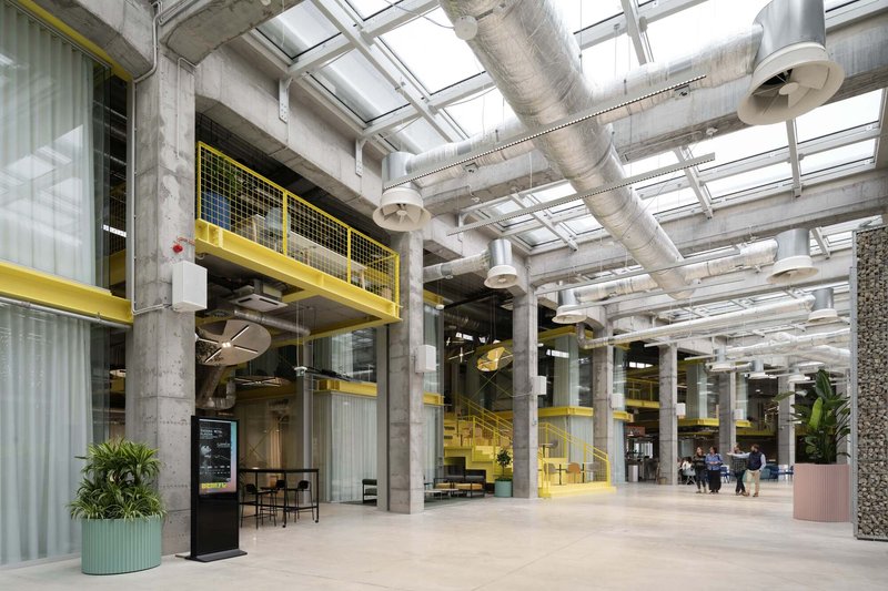 Interior atrium with exposed concrete columns, yellow mesh walkways and glazed skylight ceiling