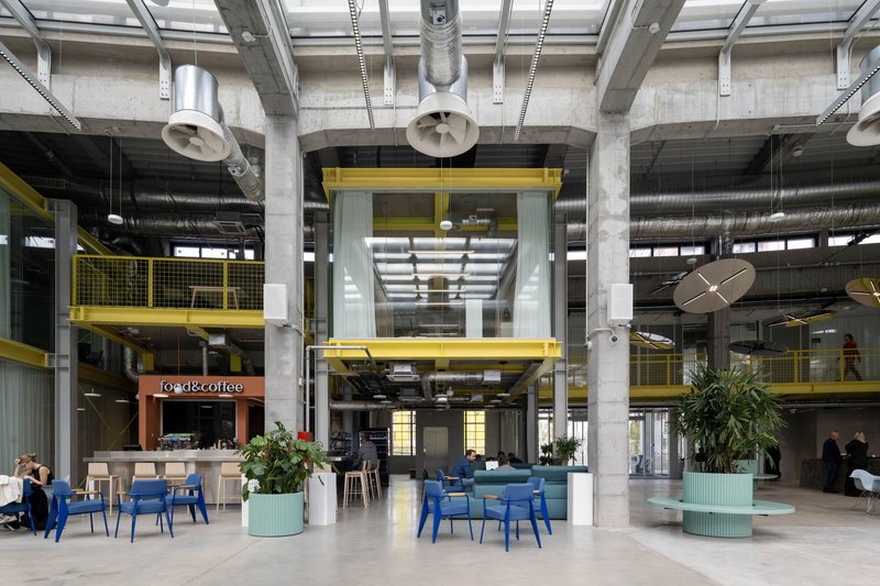Ground floor lobby space with concrete structure, yellow metal railings and planted seating areas