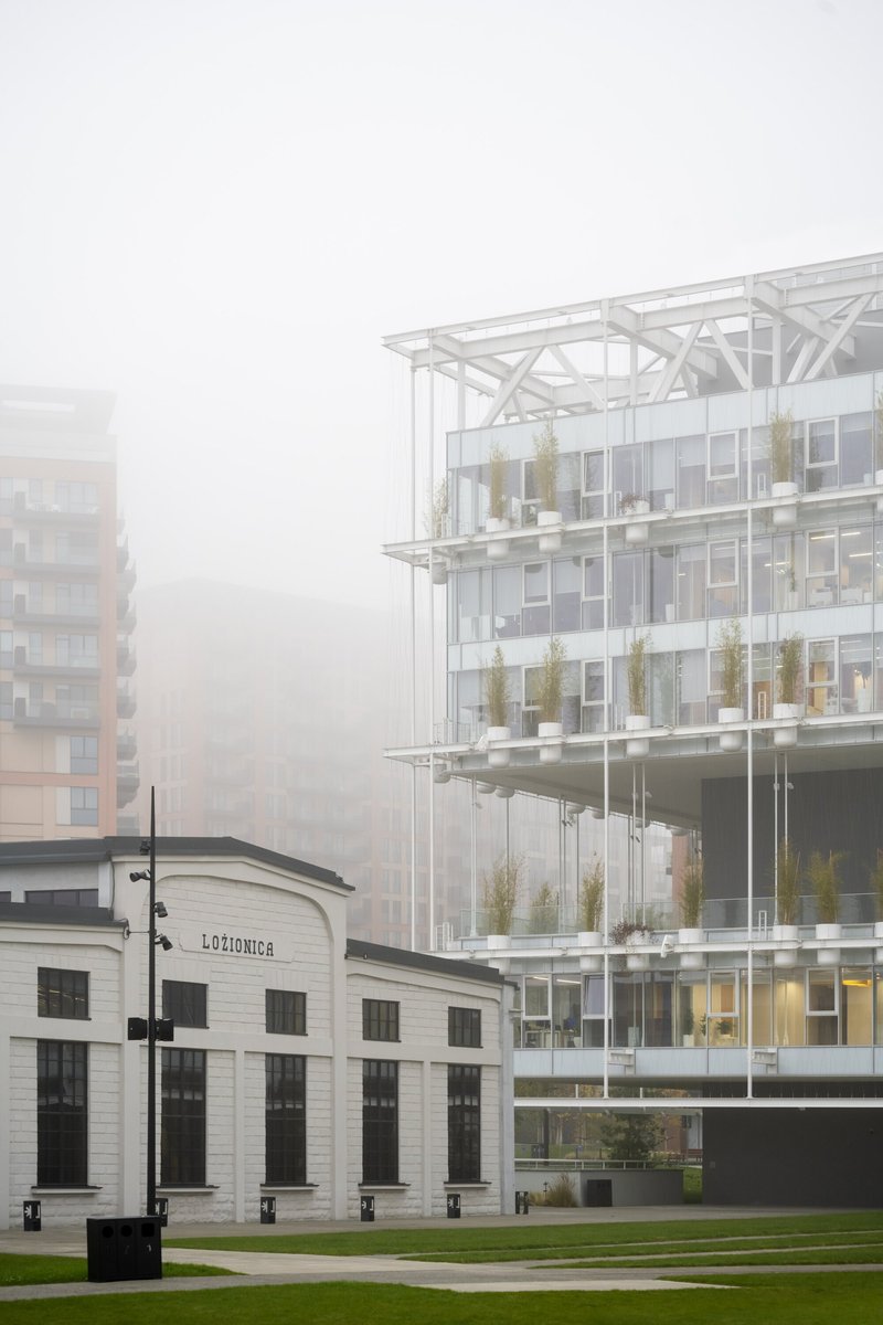 Glazed structure with exposed white truss roof rising behind a restored white masonry pavilion in mist