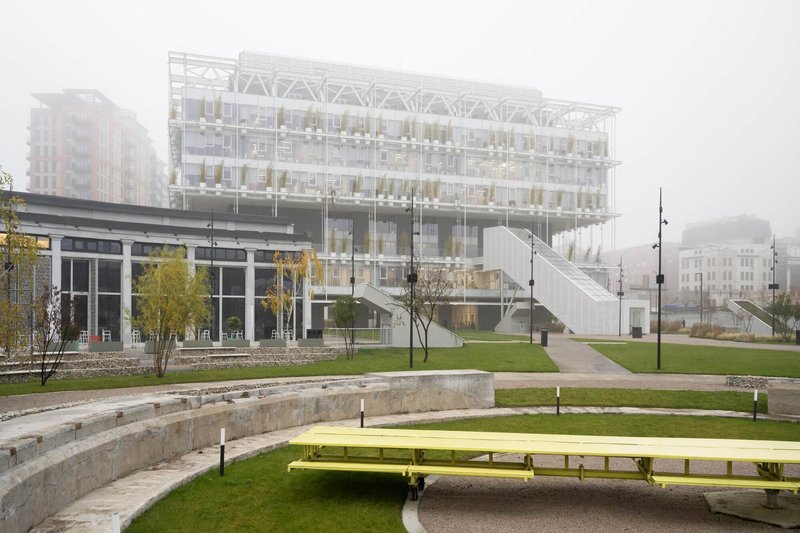 Terraced public park with yellow benches and concrete amphitheater steps leading toward the glass building