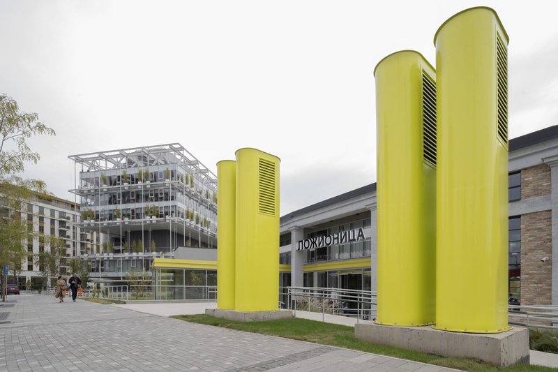 Three yellow ventilation towers with louvered openings standing in front of the plaza entrance