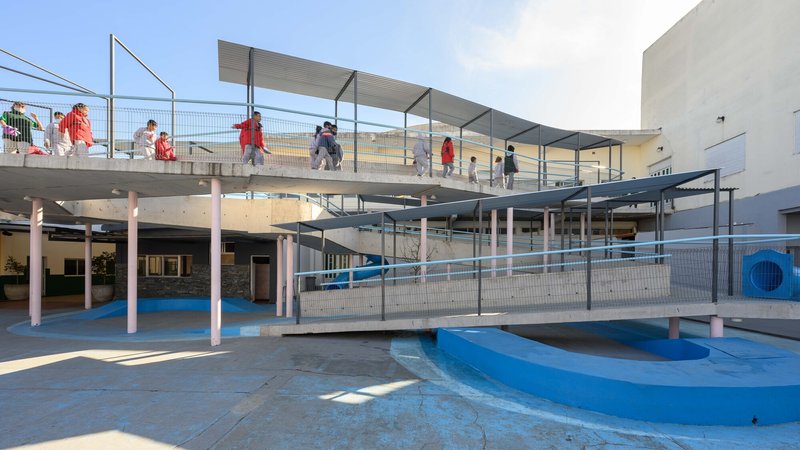 Elevated concrete ramps and walkways with wire mesh railings over a blue painted courtyard with students crossing