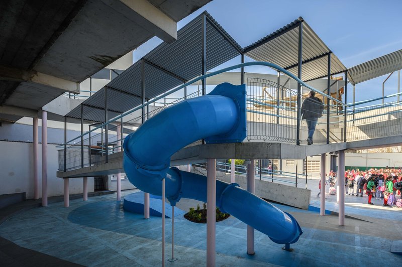 Blue spiral slide emerging from an elevated platform with metal mesh railings and concrete roof canopies