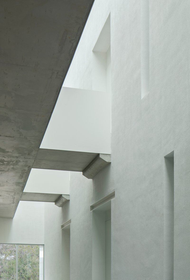 Vertical view of stacked white plaster volumes cantilevering between board-formed concrete ceilings