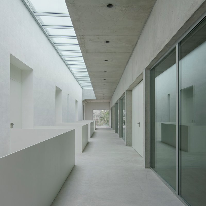 Interior corridor with continuous skylight running along concrete ceiling between white wall and glazed doors