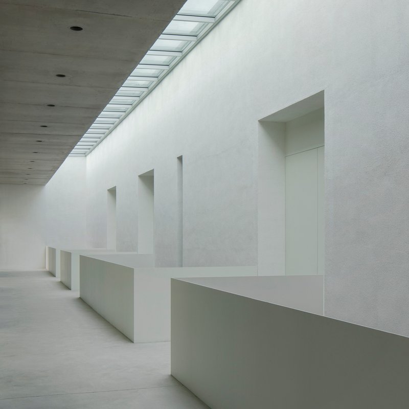 Interior hallway with recessed niches in white plaster walls beneath a linear skylight