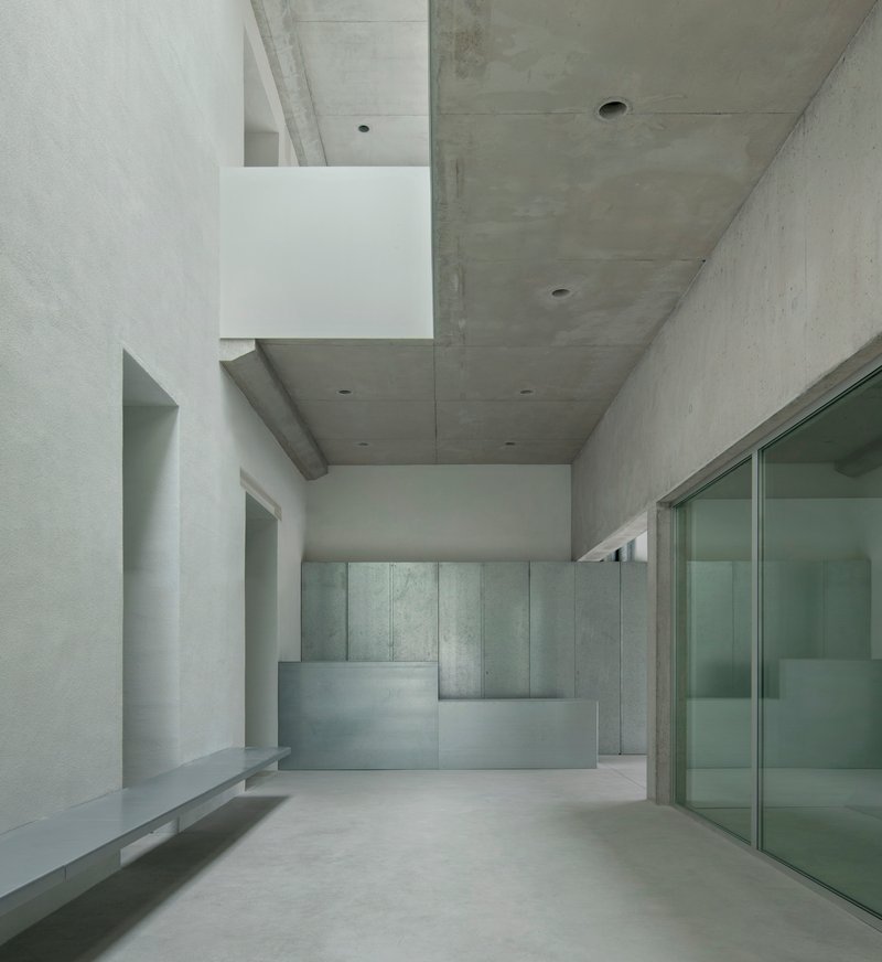 Gallery space with concrete walls and a reception desk under exposed concrete ceiling beams