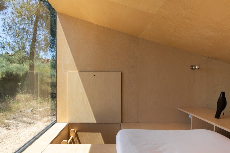 Plywood bathroom with corner glazing framing dry summer grasses and a freestanding white bathtub