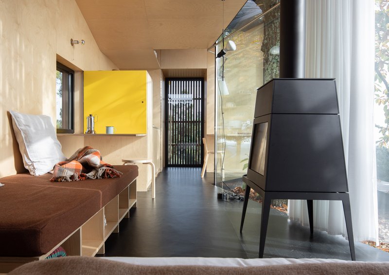 Interior living space with plywood ceiling, black metal stove, yellow cabinet, and glass wall