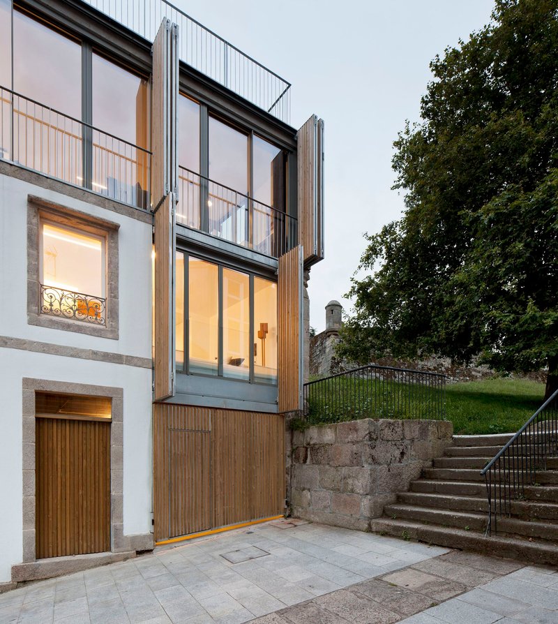 Street-level view of the vertical timber-clad extension with illuminated windows at dusk
