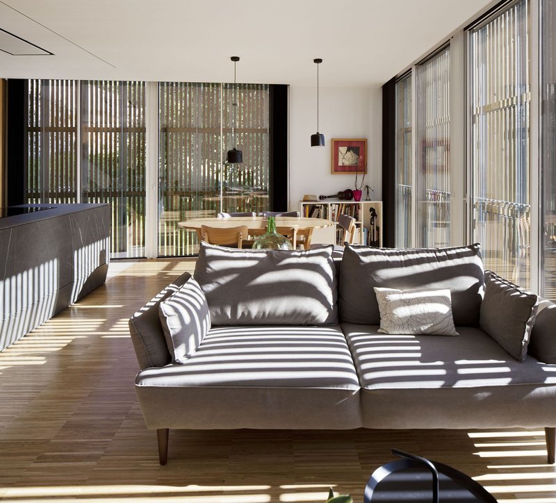 Open-plan living space with vertical timber screens filtering sunlight into geometric shadow patterns