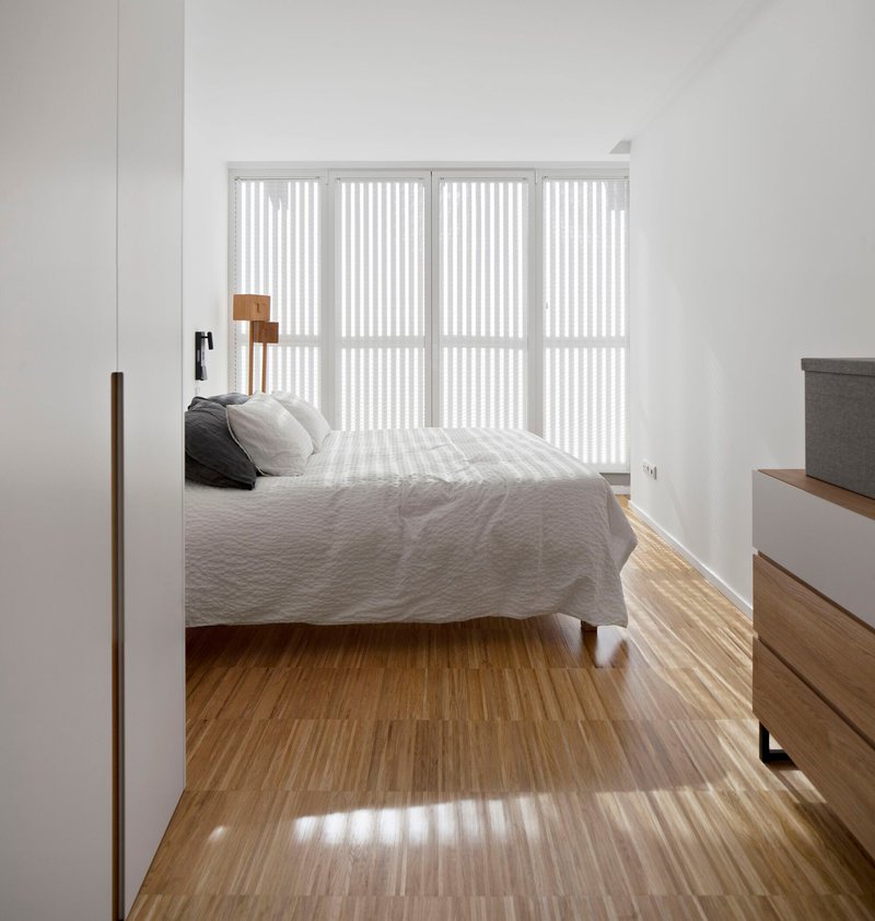 Bedroom view through a timber-framed doorway with vertical blinds casting striped shadows on the floor