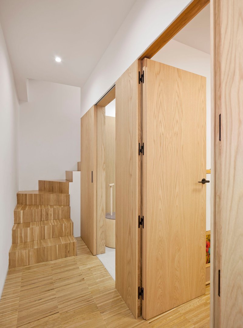Light oak staircase and flush door beneath a sloped ceiling in a narrow corridor