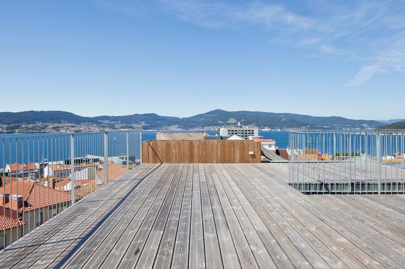 Rooftop timber deck with vertical slat railing overlooking a bay and distant hills