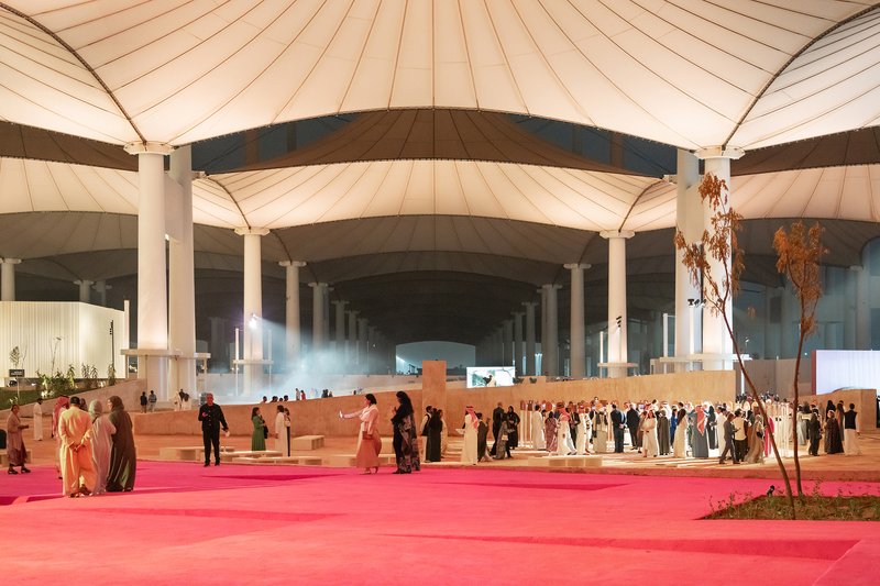 Gathering of people on a pink carpet runner beneath the radial canopy structure at dusk