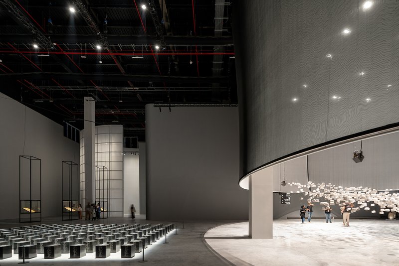 Interior auditorium with curved balcony, exposed black ceiling infrastructure, and rows of dark seating cubes