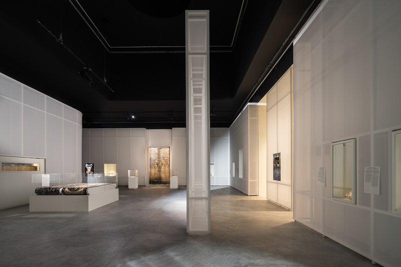 Gallery space with white partition walls, black ceiling, and tall white column beneath track lighting