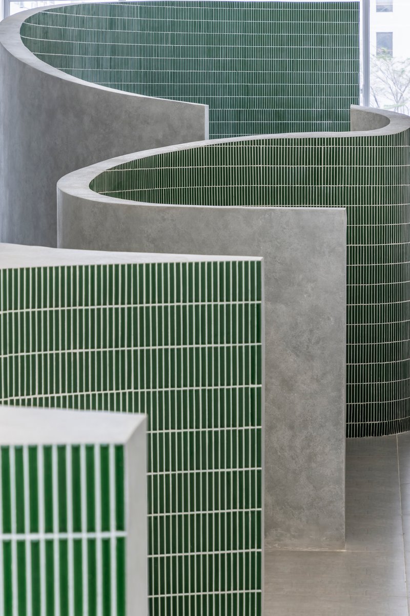 Close view of overlapping curved concrete walls clad with horizontal green ceramic tile strips
