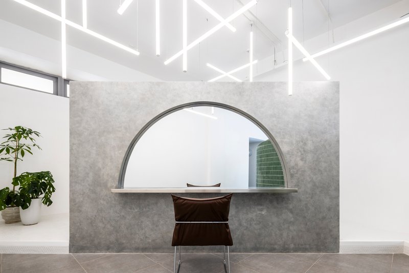 Reception desk with arched opening in grey concrete wall beneath linear ceiling lighting fixtures