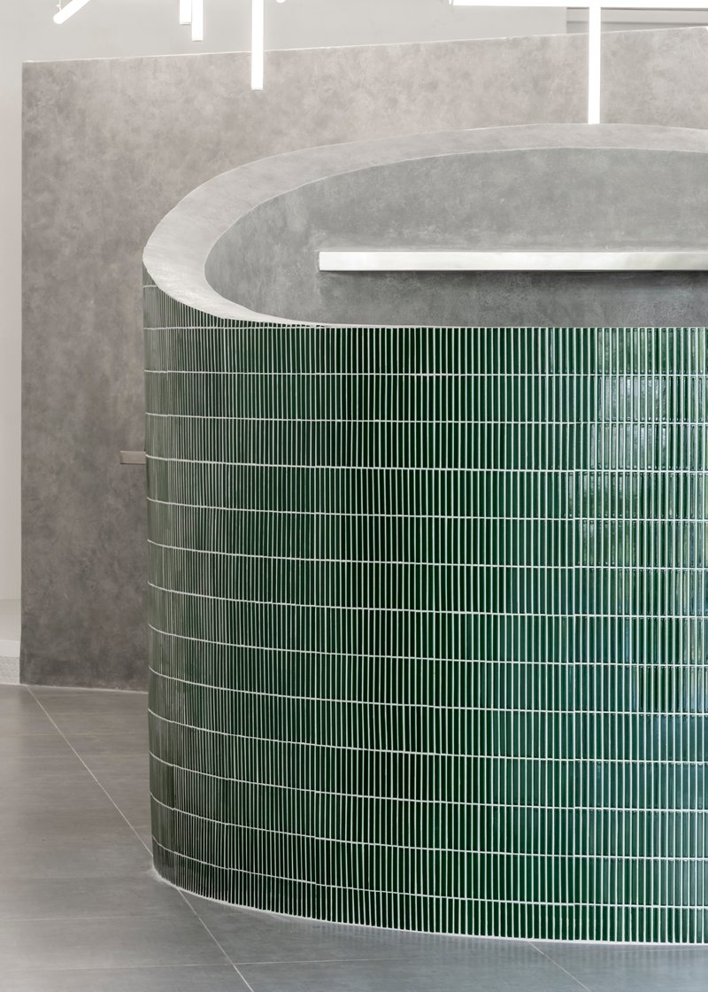 Curved counter clad in vertical green ceramic tiles beneath a concrete soffit