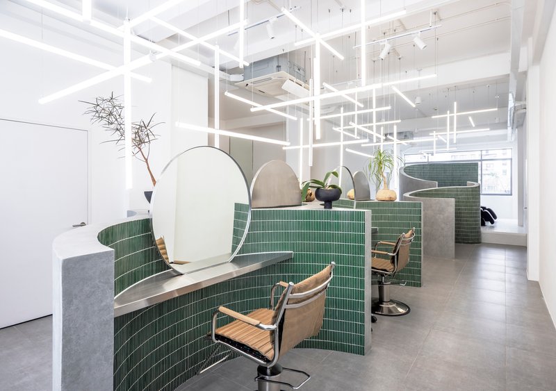 Salon interior with green mosaic tile partitions and arched mirrors beneath a white linear lighting grid