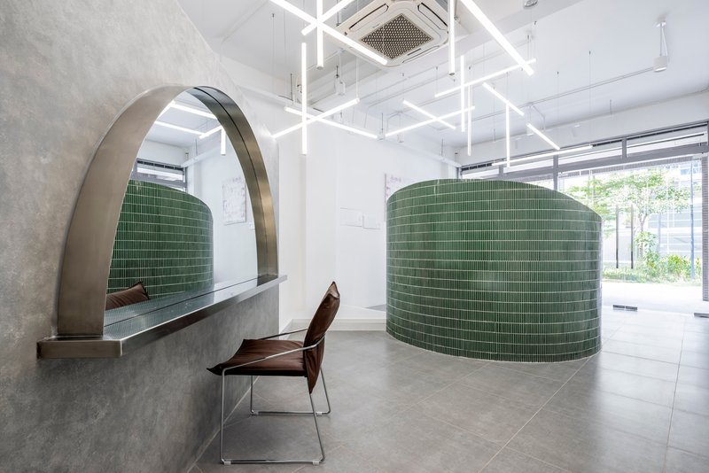 Curved green tile wall with arched concrete canopy and a wooden chair near daylit storefront windows