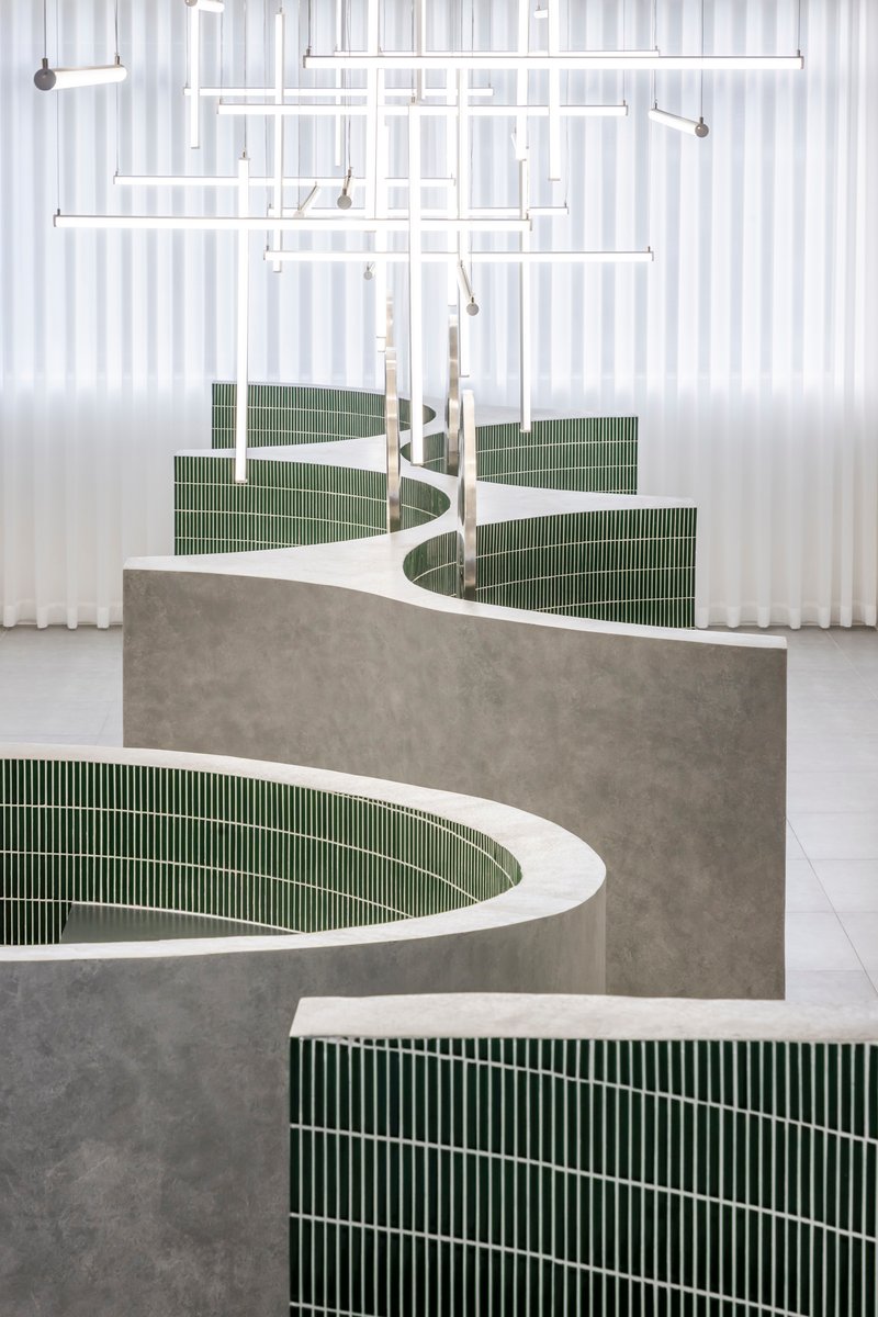 Close-up of curved concrete countertop with green mosaic tile base and white resin top under sheer curtains
