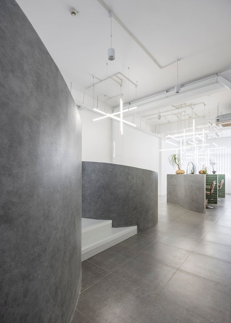 Curved concrete reception desk with built-in bench seating beneath exposed white ceiling and linear lighting
