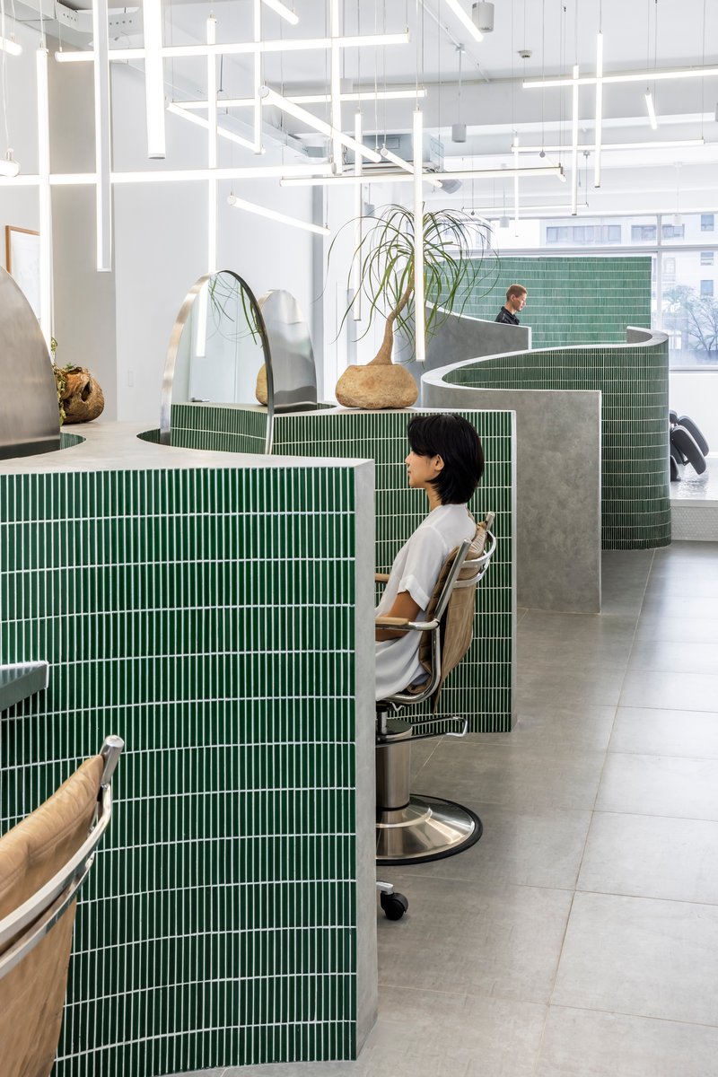 Green mosaic tile partition walls with curved concrete tops separating salon workstations