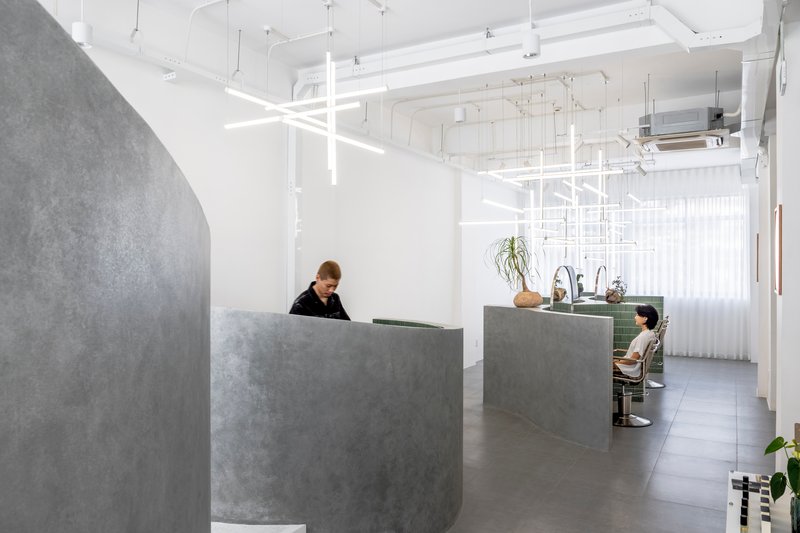 Reception area with curved concrete desk under suspended white linear lighting grid and sheer curtains
