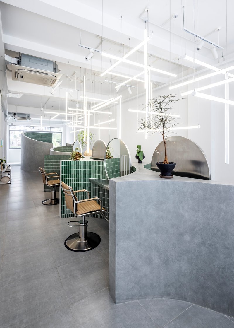 Salon workstations with green tile partitions, curved concrete screens and potted plants under grid lighting