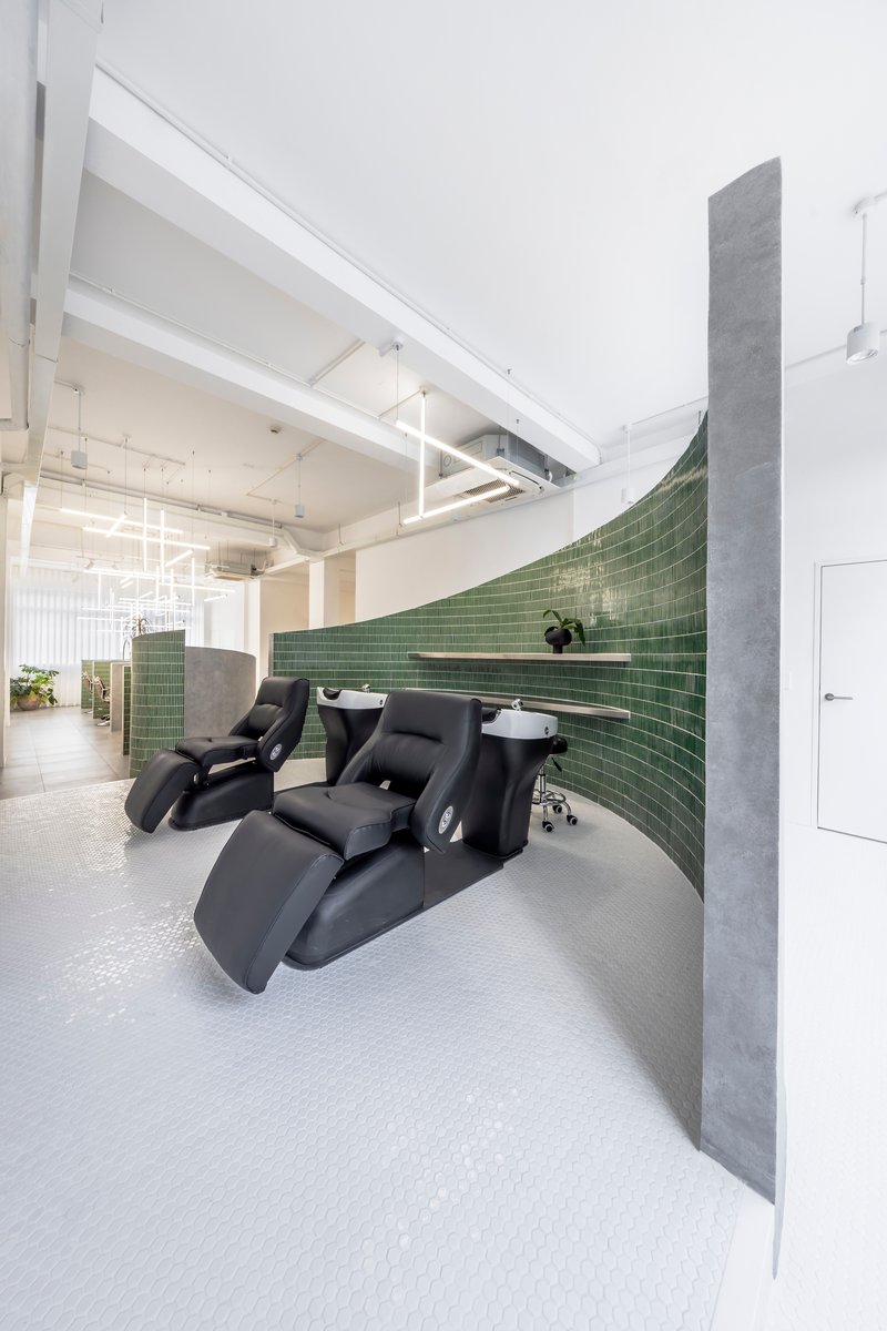 Salon interior with black reclining chairs against a curved green tile wall beneath exposed ceiling beams
