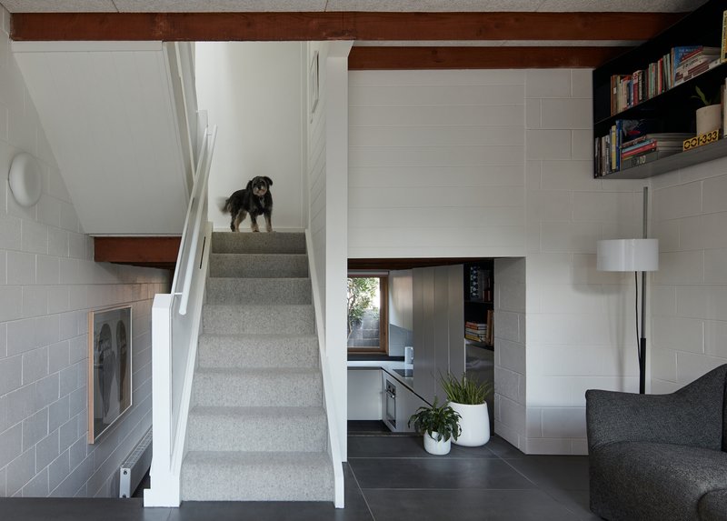 Interior staircase with grey tile walls, exposed timber beams, and a dog standing on the landing