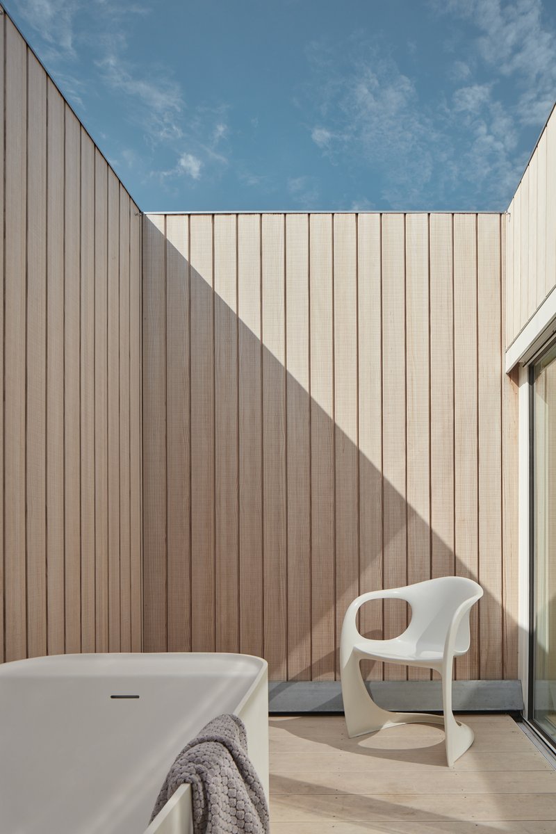 Rooftop courtyard with vertical timber cladding walls casting shadows under open sky