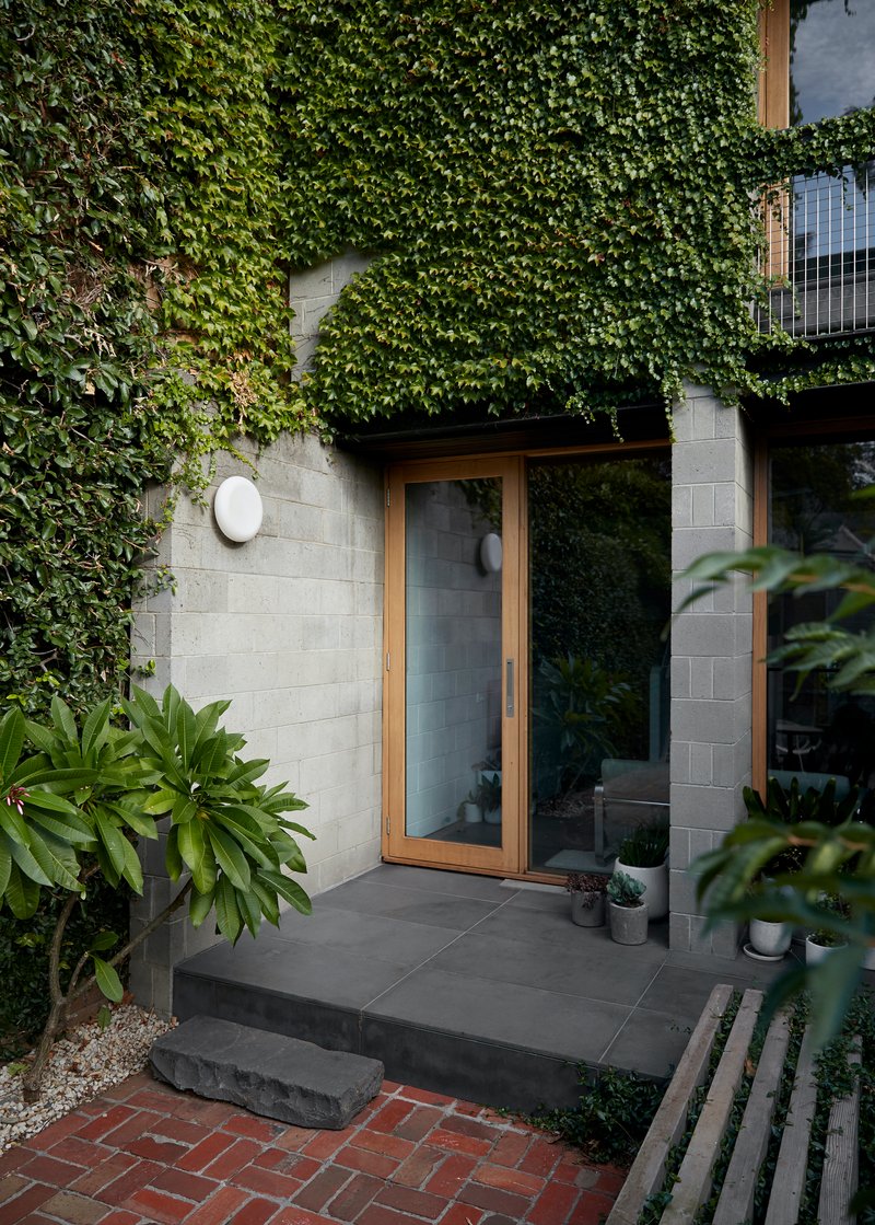 Ground-level courtyard with concrete block walls draped in ivy and glazed doors opening to interior