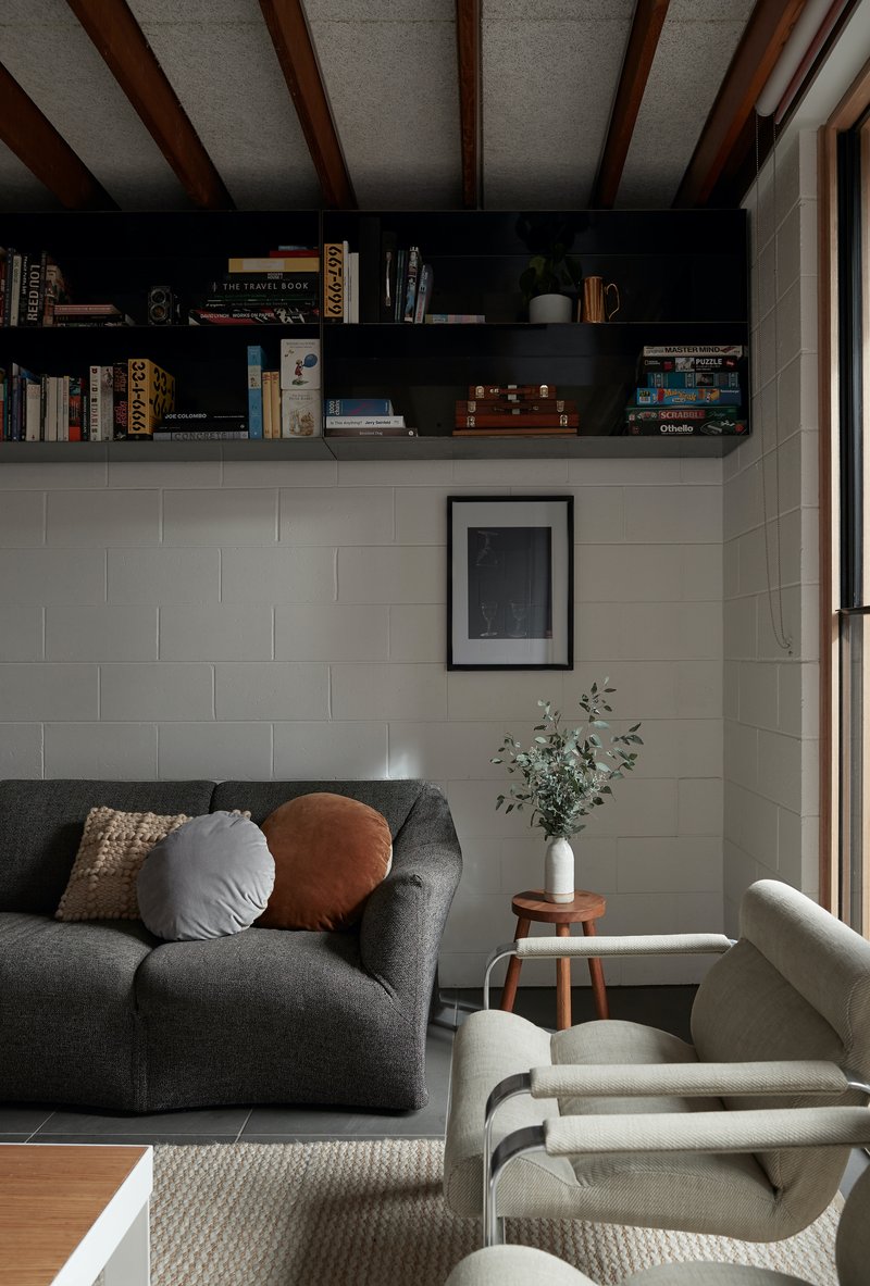 Living room with exposed timber ceiling beams and white brick wall below open bookshelves