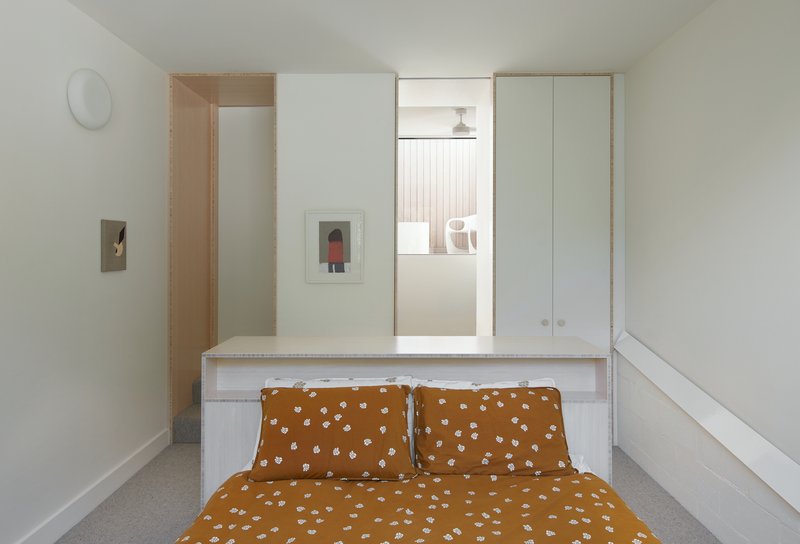 Bedroom with plywood-edged partition and doorway glimpse to bathroom with timber slats beyond