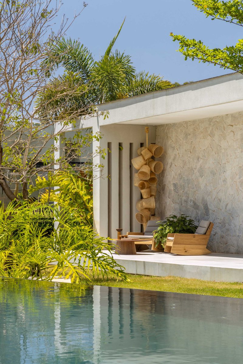 Covered terrace with stone wall and timber seating overlooking a reflecting pool edged with lawn