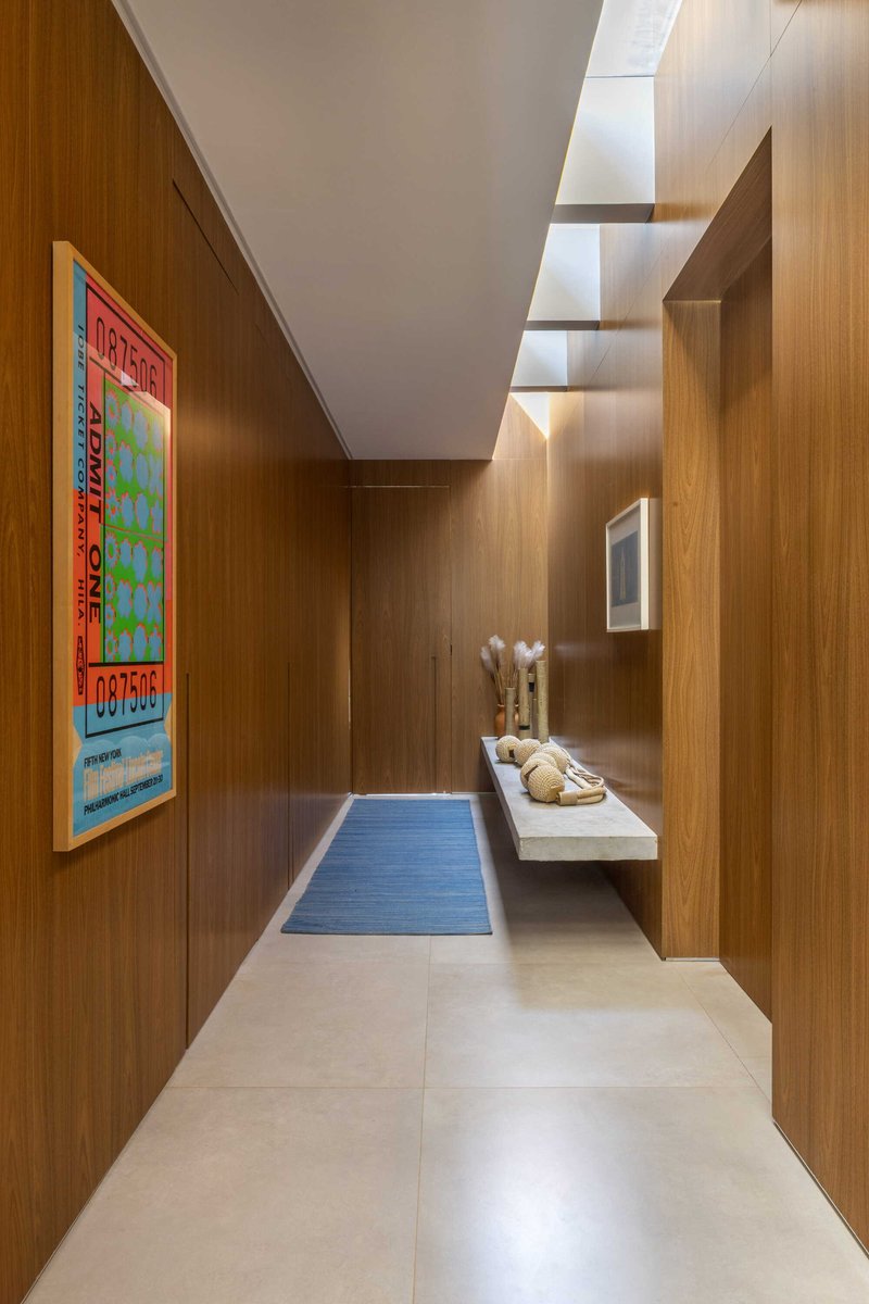 Narrow hallway with wood paneled walls, recessed ceiling lighting and pale stone floor