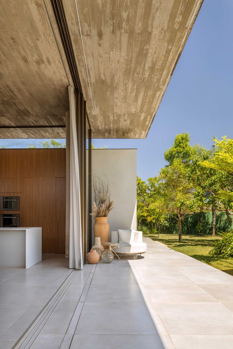 Covered terrace with board-marked concrete soffit opening to a lawn with green trees beyond