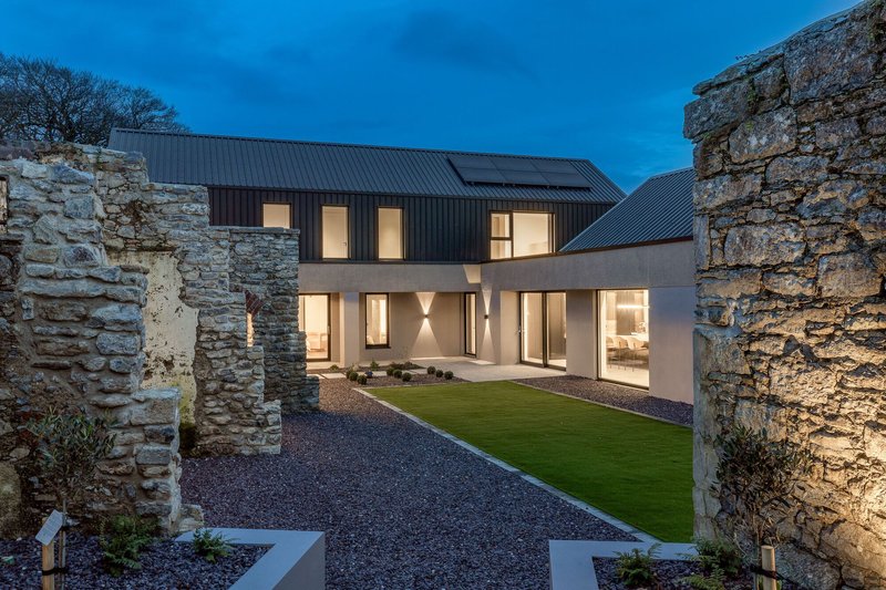 Gravel courtyard framed by illuminated stone ruins and the glazed facade at dusk