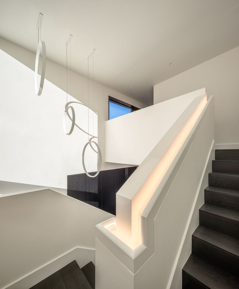 White stairwell with integrated LED handrail and sculptural ribbon pendant fixture suspended in the void
