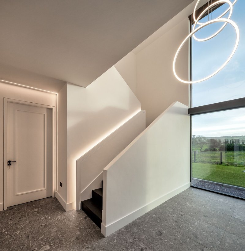 Entry hall showing illuminated stair balustrade and floor-to-ceiling glazing overlooking green fields