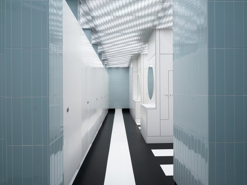Interior corridor with blue tile walls, black and white striped floor beneath a grid ceiling skylight