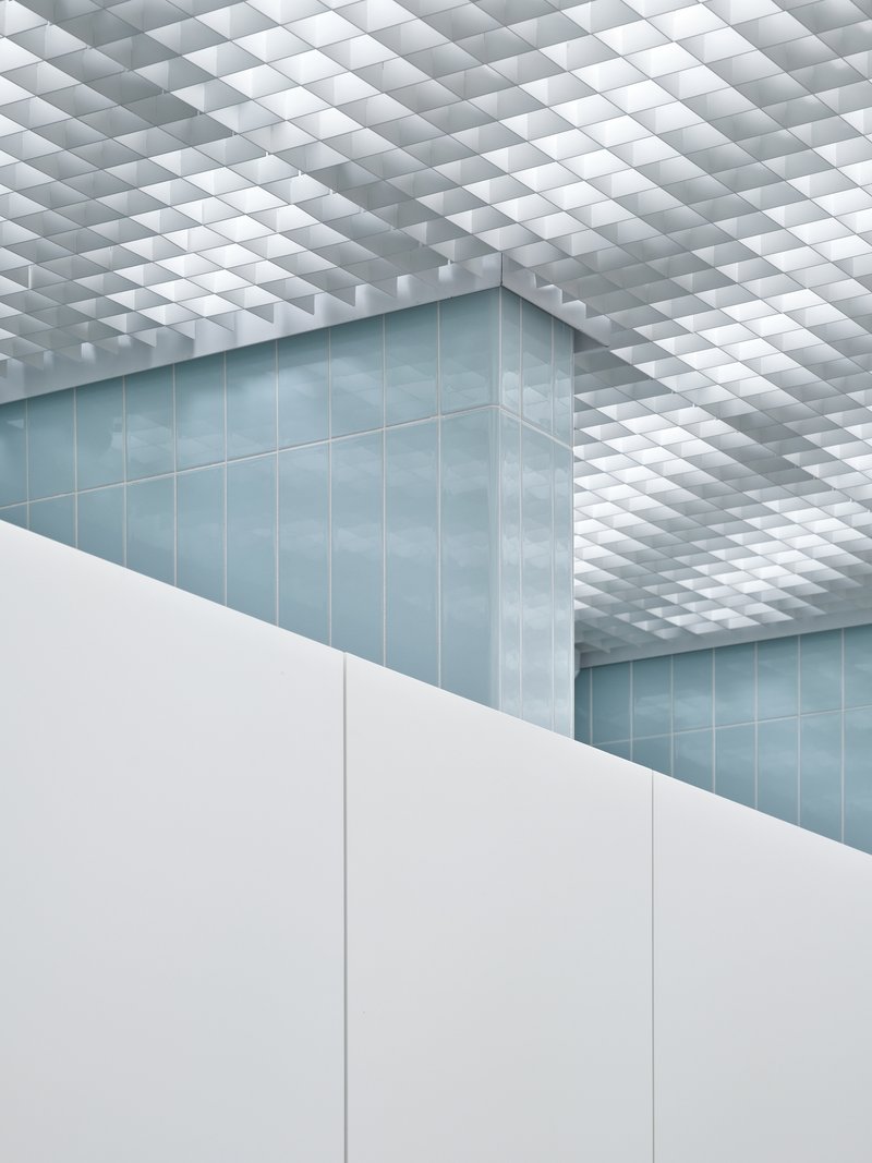 Corner view of blue tiled wall beneath a white pyramidal grid ceiling